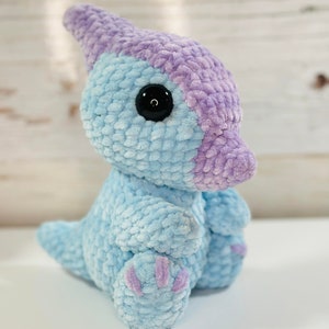 May include: A light blue and purple crocheted dinosaur plush toy with black eyes.