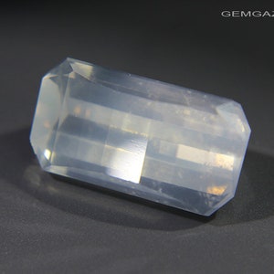 May include: A clear, faceted, rectangular gemstone with a slightly cloudy appearance. The gemstone is cut in a rectangular shape with beveled edges.
