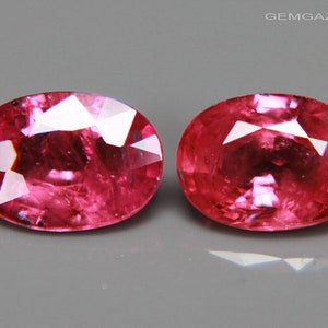 Könnte beinhalten: Zwei ovale rosafarbene Edelsteine mit facettiertem Schliff. Die Edelsteine sind vor einem grauen Hintergrund platziert.