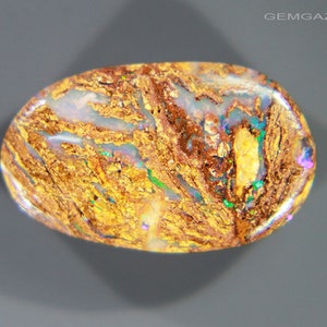 May include: A golden brown opal cabochon with iridescent flashes of blue, green, and purple. The opal has a rough, textured surface.