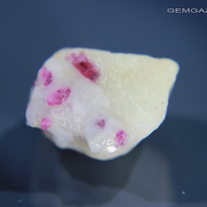 May include: A small, white rock with several small, pink crystals embedded in it.