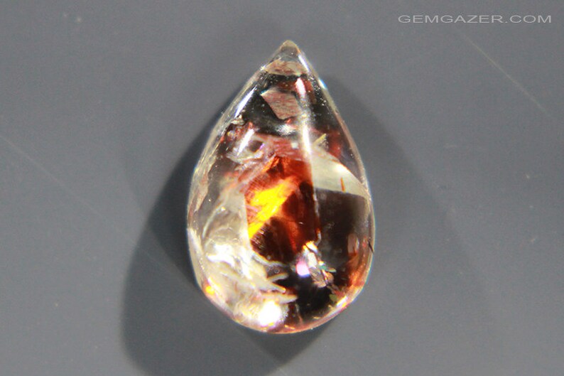 Pu&ograve; includere: Una pietra preziosa trasparente a forma di lacrima con inclusiones di rosso, arancione e giallo. La pietra preziosa &egrave; sfaccettata e ha un'alta lucidatura.