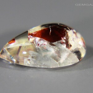 Pu&ograve; includere: Una pietra preziosa a cabochon a forma di lacrima con un corpo chiaro e traslucido e inclusiones di rosso, bianco e oro. La pietra preziosa ha una superficie liscia e lucidata.