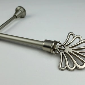 May include: A silver-coloured curtain rod with a decorative, fan-shaped finial. The rod includes a bracket and a separate, smaller rod with a rounded end. The design is modern and suitable for various home decor styles.