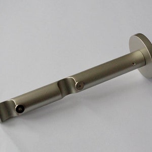Könnte beinhalten: Silberfarbener Gardinenstangenhalter mit kreisförmiger Montageplatte und zylindrischer Stange. Die Stange hat eine geschwungene Form und ein kleines Loch für eine Schraube. Der Halter aus Metall dient zur Befestigung einer Gardinenstange.