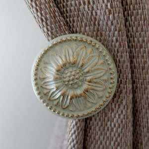 May include: A decorative curtain tieback with a floral design. The tieback is made of metal and has a light green finish with gold accents.