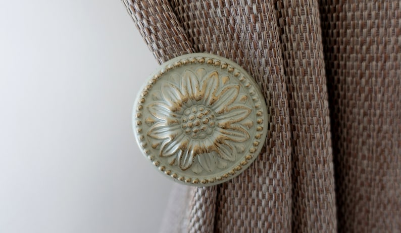 May include: A decorative curtain tieback with a floral design. The tieback is made of metal and has a light green finish with gold accents.