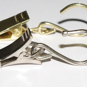 May include: Two metal curtain clips, one gold and one silver, connected by a chain. The silver clip has a hook on the end.