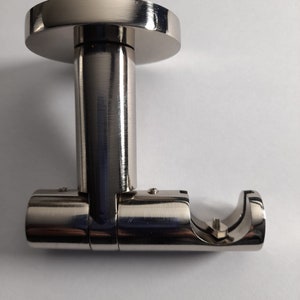 May include: A brushed nickel curtain rod bracket. The bracket has a circular base, a cylindrical post, and a curved cradle to hold the rod. The metal has a shiny, reflective surface, and the design is modern and minimalist.