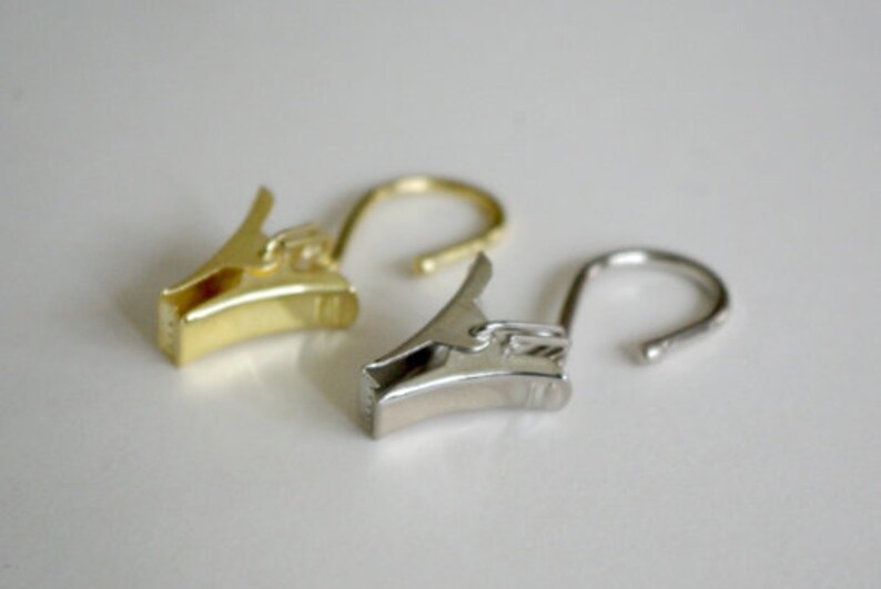 May include: Two curtain clips, one gold and one silver, with a hook on the end.
