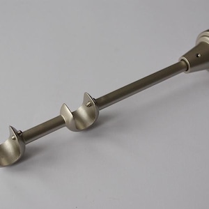 Op de afbeelding: Een gordijnroede van geborsteld nikkel met een dubbel beugelontwerp. De roede heeft een cilindrisch lichaam met een decoratieve eindkap en twee gebogen beugels. De hardware is ontworpen voor eenvoudige installatie en voegt een moderne touch toe.