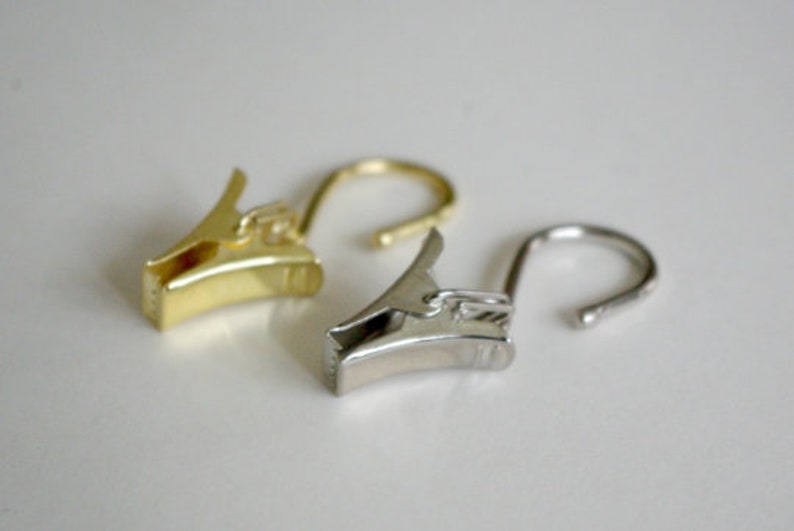 May include: Two curtain clips, one gold and one silver, with a hook on the end.
