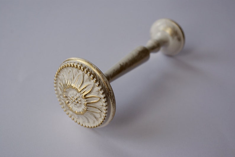 May include: White and gold decorative curtain rod finial with a floral design.