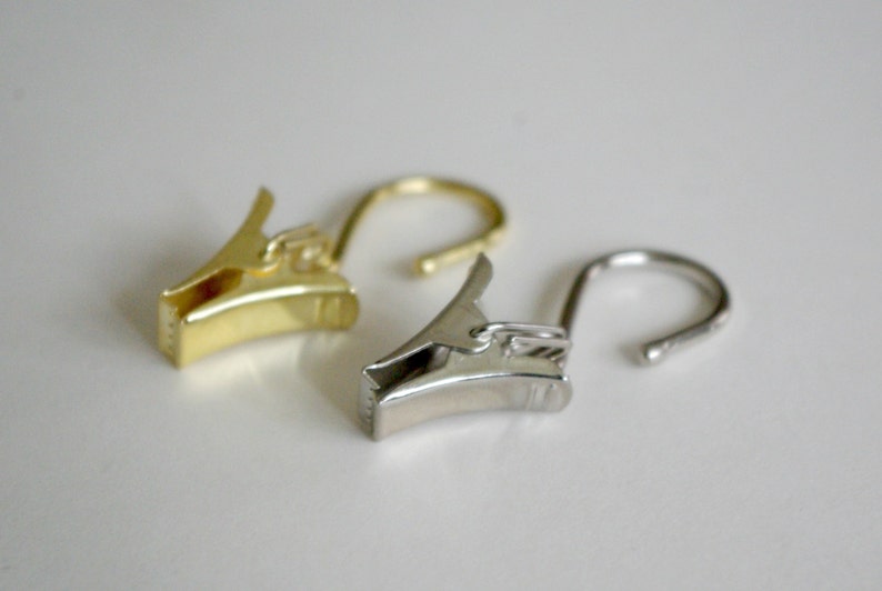 May include: Two curtain clips, one gold and one silver, with a hook on each end.