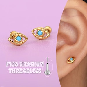 May include: Gold-colored, eye-shaped stud earrings with a turquoise center stone. The earrings are threadless and made of titanium. The image also shows the text "F136 TITANIUM THREADLESS".