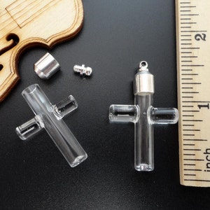 May include: Two clear glass cross shaped vials with silver caps and stoppers. The vials are approximately 1 inch in length.