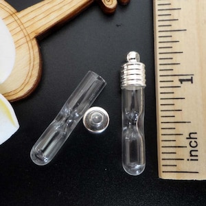 May include: Two clear glass vials with silver caps. One vial is open and the other is closed. The vials are about 1 inch long.