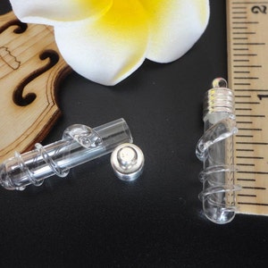 May include: Two clear glass vials with silver tops and a twisted design. The vials are approximately 1 inch long and are shown next to a ruler.