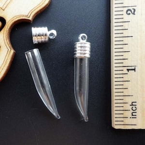 Könnte beinhalten: Zwei klare Glasfläschchen mit silbernen Kappen und eine silberne Kappe mit einer Schlaufe zum Aufhängen. Die Fläschchen sind etwa 2,5 cm lang und werden neben einem Lineal gezeigt.