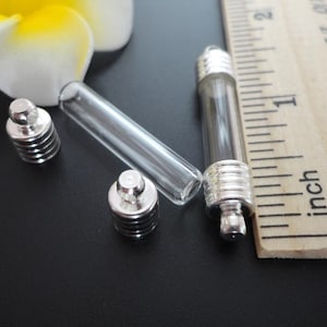 May include: Three silver-toned metal bottle stoppers with clear glass vials. The vials are approximately 1 inch long. The stoppers have a threaded design.