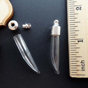Könnte beinhalten: Ein Satz aus silbernen und gläsernen Anhänger-Komponenten zum Herstellen von Schmuck. Das Set enthält ein Glasfläschchen, eine silberne Kappe, einen silbernen Verbinder und eine silberne Kugel. Das Fläschchen ist etwa 2,5 cm lang.