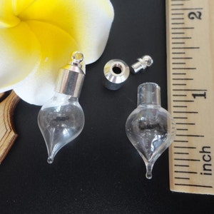 Può includere: Due bottiglie di vetro trasparente a forma di lacrima con tappi e tappi argentati. Le bottiglie sono lunghe circa 2,5 cm e sono mostrate accanto a un righello.