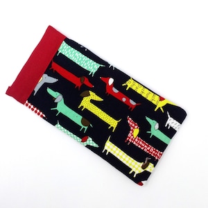 May include: A rectangular glasses case featuring a black background with a repeating pattern of colourful dachshund dogs. The top edge is solid red fabric. The case is designed to hold glasses.