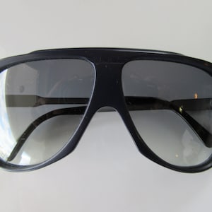 K&ouml;nnte beinhalten: Eine schwarze Aviator-Sonnenbrille mit dunkelgrauen Gl&auml;sern.