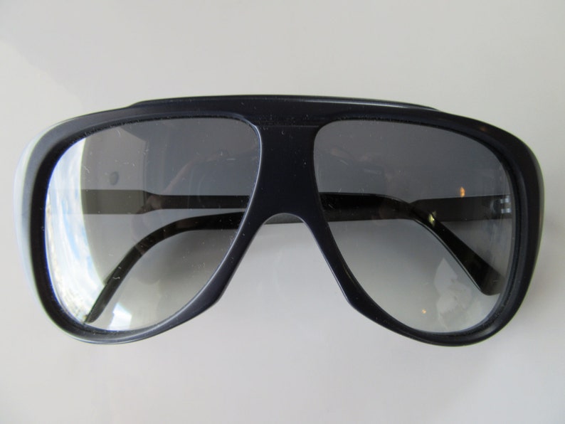 K&ouml;nnte beinhalten: Eine schwarze Aviator-Sonnenbrille mit dunkelgrauen Gl&auml;sern.