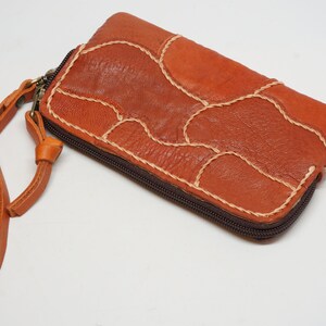 Puede incluir: Una cartera de cuero marrón con cierre de cremallera y una correa larga. La cartera está hecha de varias piezas de cuero cosidas juntas en un diseño de patchwork.