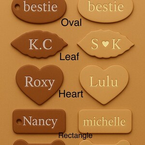 May include: A selection of pet name tags in various shapes and colors. The tags are tan and natural, with names like "bestie," "Roxy," and "Sydney." Shapes include oval, leaf, heart, rectangle, and bone.