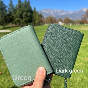 May include: Two small, zippered wallets in shades of green. One is a lighter green, labeled "Green", and the other is a darker green, labeled "Dark green". Both wallets have a textured surface and a zipper closure.