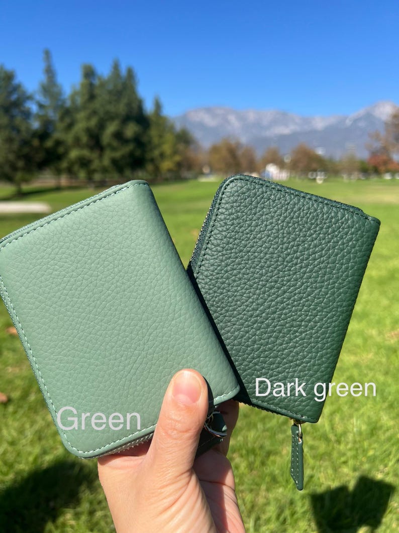 May include: Two small, zippered wallets in shades of green. One is a lighter green, labeled "Green", and the other is a darker green, labeled "Dark green". Both wallets have a textured surface and a zipper closure.