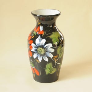 Peut inclure: Vase en céramique noire avec un bord intérieur blanc. Le vase est orné de fleurs peintes à la main en blanc, orange et vert. Le motif floral est posé sur un fond noir.