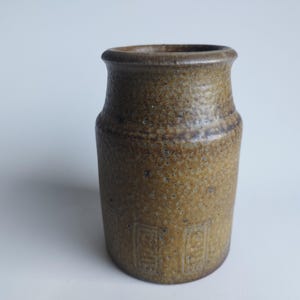 May include: A brown ceramic vase with a textured surface and a geometric pattern. The vase is approximately 4 inches tall.