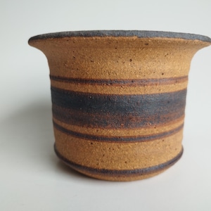 May include: A brown ceramic planter with black stripes. The planter has a wide, rounded rim and a textured surface.