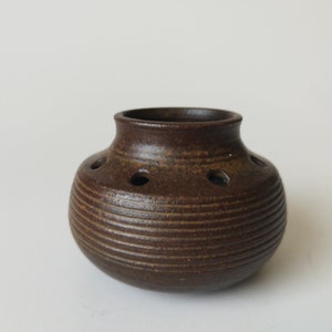 May include: A brown ceramic vase with a ribbed texture and small holes around the top. The vase is designed to hold flowers.