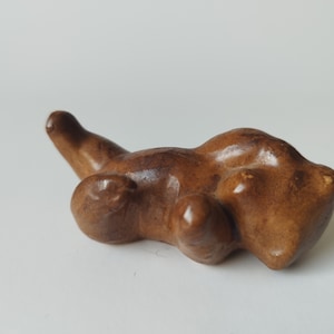 Könnte beinhalten: Eine kleine, braune Keramikfigur eines Bären, der auf dem Rücken liegt und seine Pfoten in die Luft streckt.