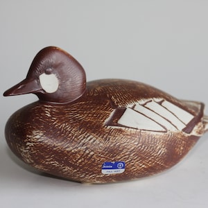 May include: A brown ceramic duck figurine with white markings. The duck has a detailed design and a label on the bottom that reads "JENSEN PAUL HOFF".
