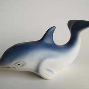 Puede incluir: Una figurita de cerámica de un delfín azul y blanco, con un acabado liso y brillante. El delfín está nadando con la cola levantada.