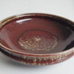 May include: A red ceramic bowl with a speckled glaze. The bowl has a wide rim and a deep, rounded interior.