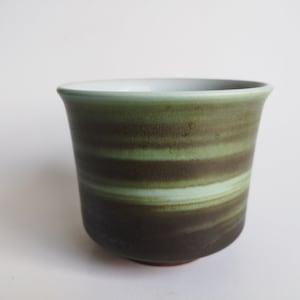 May include: A green and brown ceramic cup with a white interior. The cup has a striped pattern.