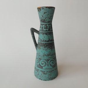 May include: A tall, turquoise vase with a handle, featuring a textured surface and decorative patterns. The vase has a flared top and a narrow base. The design includes bands of geometric and scroll-like motifs, with a dark gray color contrasting the turquoise.