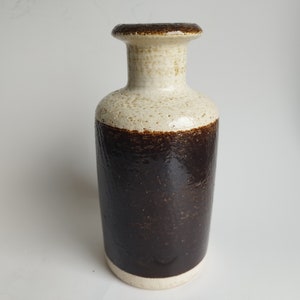 Könnte beinhalten: Eine Keramikvase mit einem weißen Oberteil und einem dunkelbraunen Boden. Die Vase hat eine strukturierte Oberfläche und eine abgerundete Form.