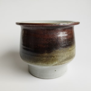 May include: A brown and green ceramic pot with a white rim and base. The pot has a glazed finish and a rounded shape.