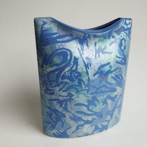 May include: A blue ceramic vase with a wavy, abstract design. The vase has a light blue and white crackle glaze with a metallic sheen.