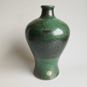 May include: A green ceramic vase with a speckled glaze. The vase has a wide base and a narrow neck.