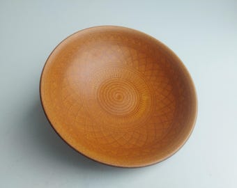 May include: A round, brown ceramic bowl with an intricate, geometric pattern etched into the interior. The bowl's design features concentric circles and diamond shapes, creating a textured surface. The bowl is a warm, earthy tone.