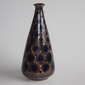 Può includere: Un vaso alto in ceramica marrone con un motivo geometrico blu e bianco. Il vaso ha un collo stretto e una base larga.