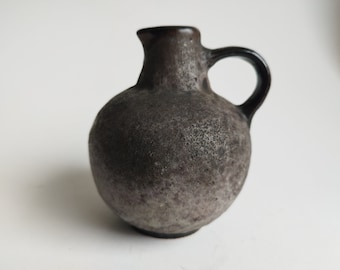 May include: A small, round, gray ceramic vase with a black handle. The vase has a textured surface.